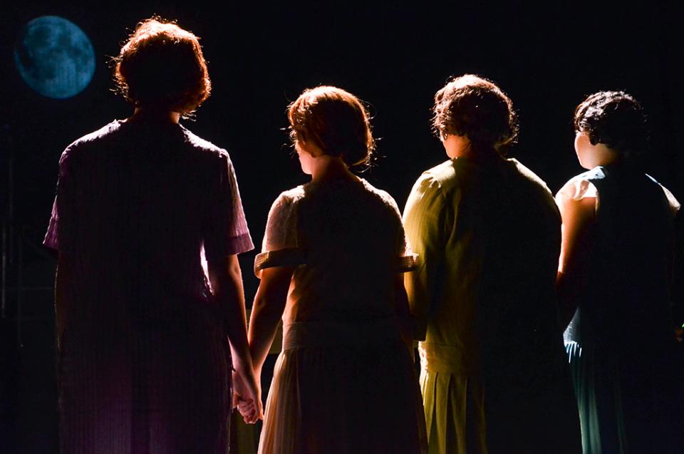 Four women holding hands, backlit, facing away from us.
